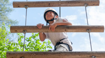 A child wearing a helmet climbing up a ladder on the ropes course.