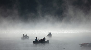 A black and white view of people canoeing on a lake.