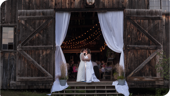 A married couple sharing a kiss at the entrance of a barn.