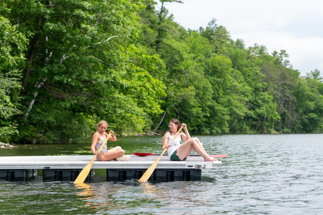 Campers learning how to canoe with paddles on the docks.