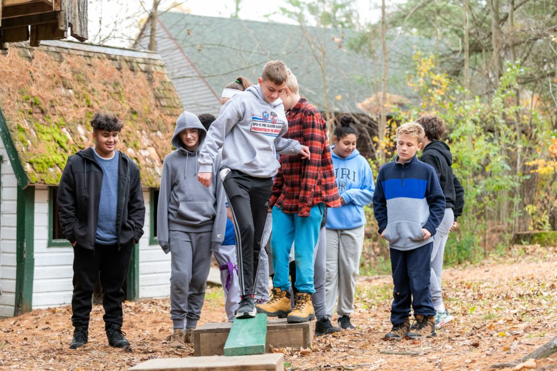 A camper walking on a balance beam as other campers wait in line.
