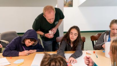 An instructor watches a student work on a project.