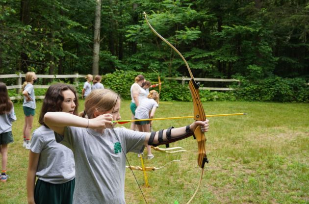 A camper learning how to shoot a bow and arrow.