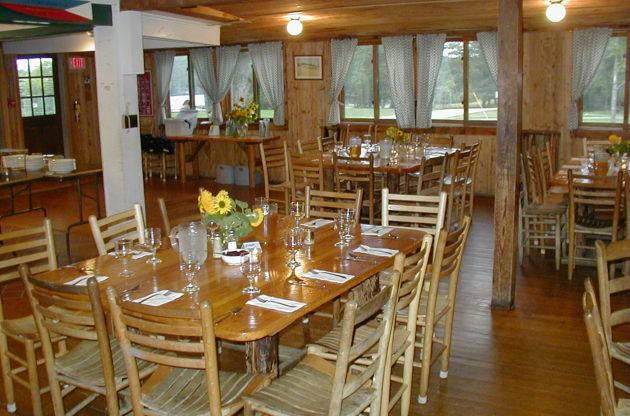 Photo of the Lanakila dining hall tables set with formal glasswear and yellow flower center pieces.