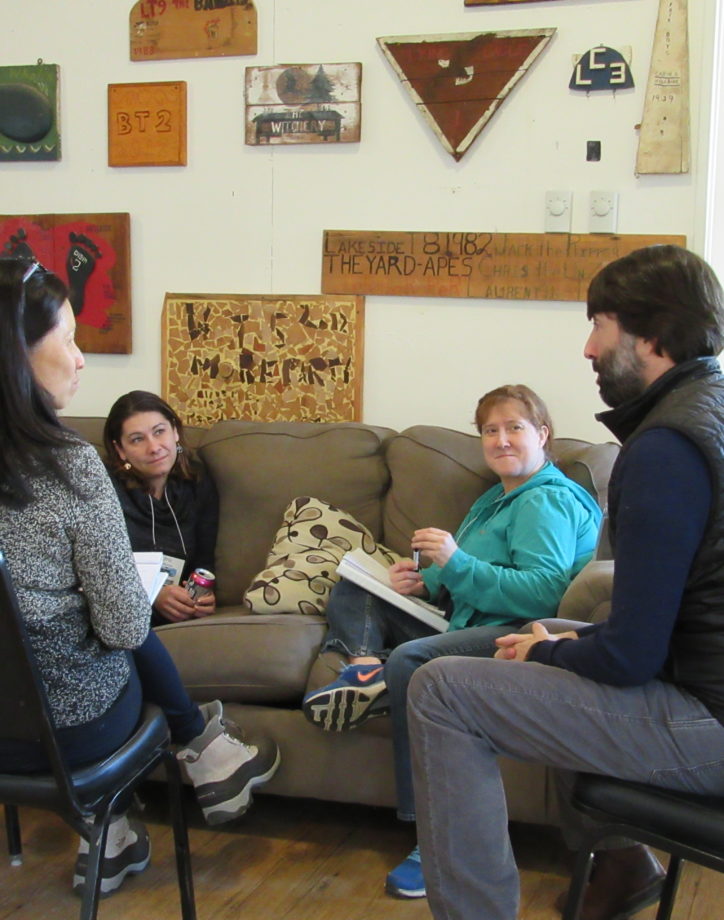 A group of four people sitting on chairs and a couch talking.