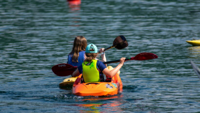 Two people are kayaking on a body of water, one in a yellow kayak and the other in an orange kayak.