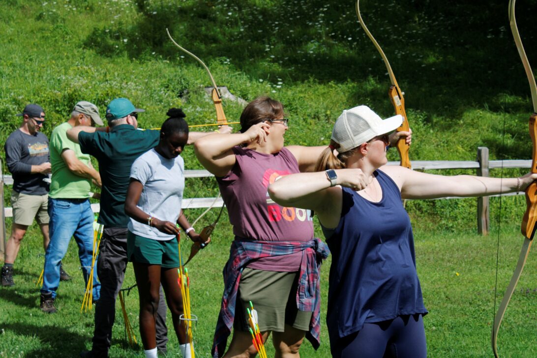 A group of people engaging in archery outdoors, each holding a bow and arrow while practicing their aim.