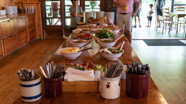 A buffet table is set up with various dishes, cutlery, and napkins in a wooden dining room.